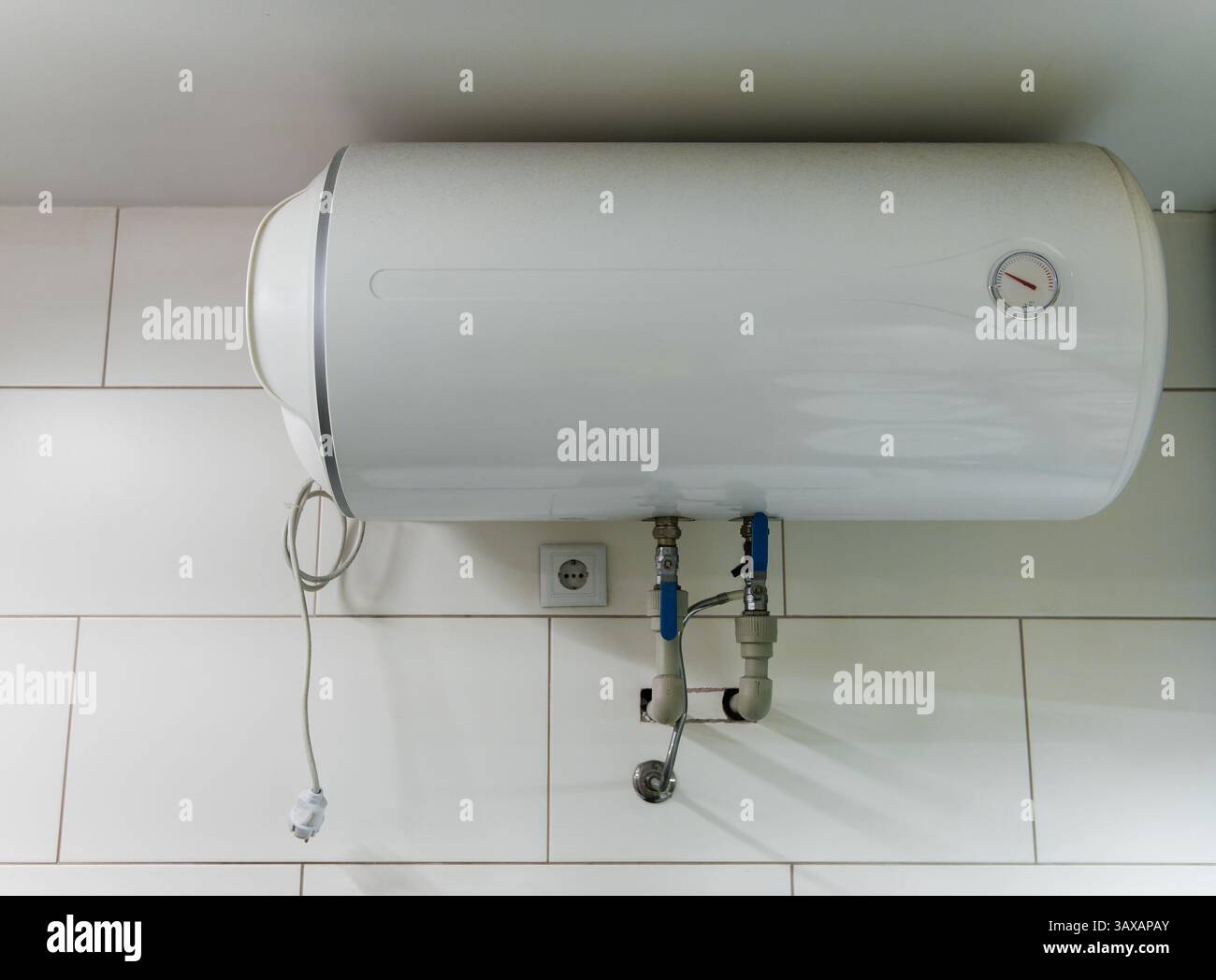 Scaldabagno elettrico montato orizzontalmente su una parete piastrellata bianca con il cavo di alimentazione scollegato Foto Stock