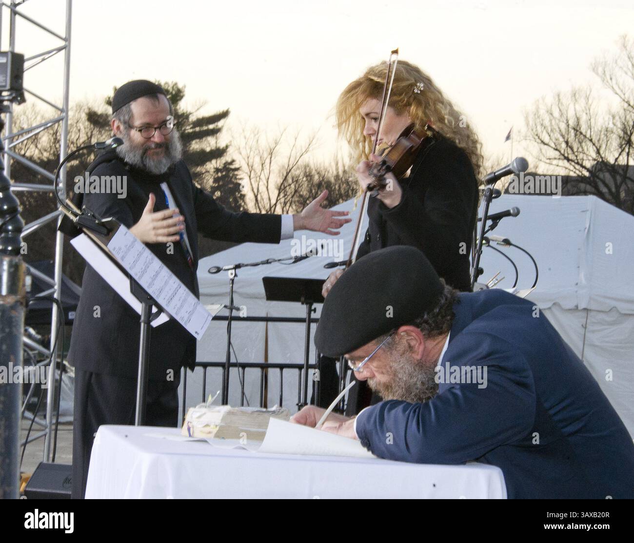 25 dicembre 2016 - Washington, District of Columbia, Stati Uniti d'America - Sofer (scriba rituale ebreo) Shaul Bassel, centro inferiore, scrive la parola nella ''Washington Torah'' usando un argilla e inchiostro di stile antico, mentre il Maestro Avremi Gourarie, a sinistra, dirige la National Menorah Orchestra, con il vincitore del Grammy Award Miri Ben Ari, centro superiore, che presenta una versione speciale di ''Hanerot Halalu'''''''''''', riferendosi alla cerimonia di illuminazione della Sacorah' on the Ellipse a Washington, DC il 25 dicembre 2016..Credit: Ron Sachs / CNP (Cre Foto Stock