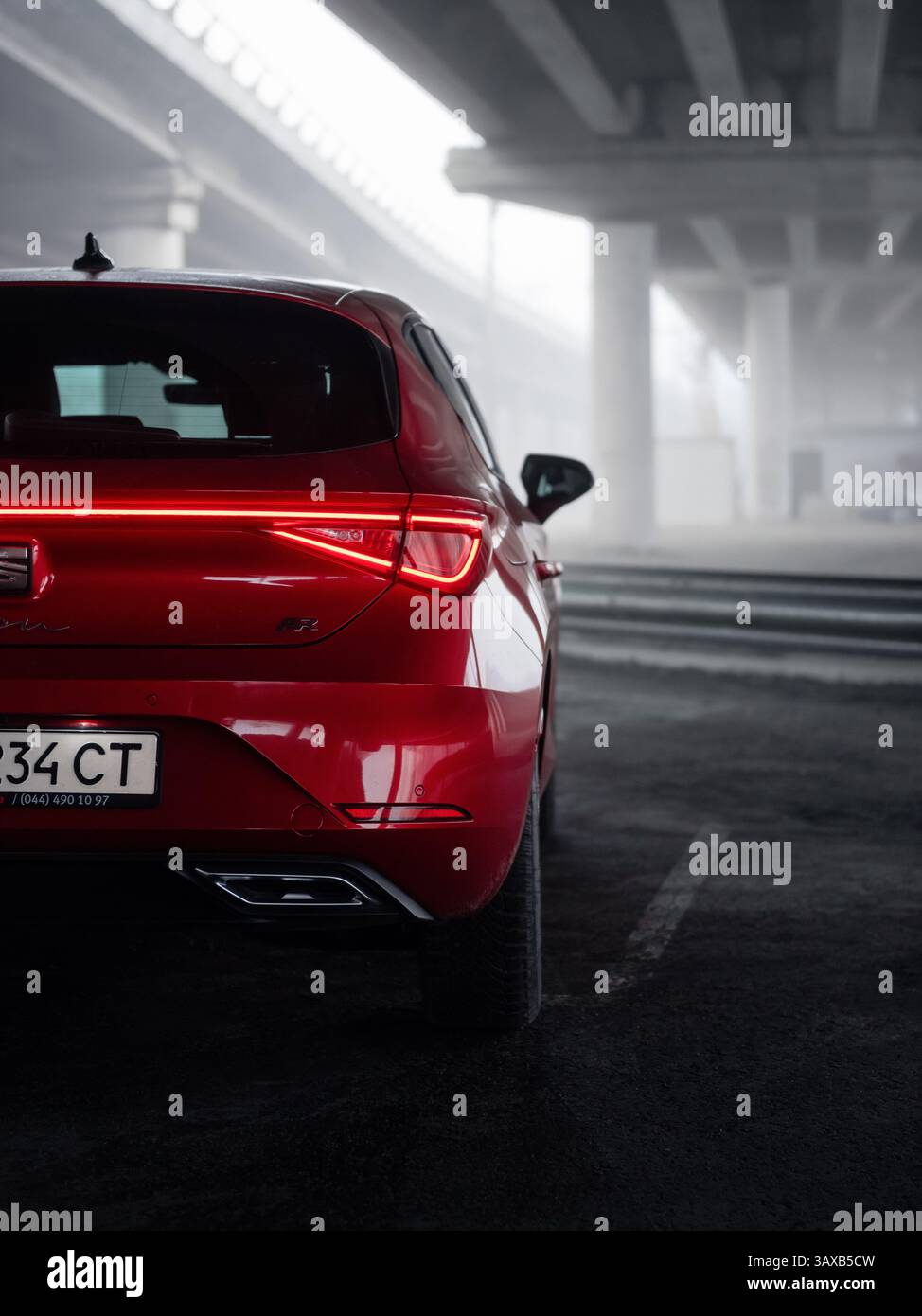 POSTO rosso Leon sotto un ponte in mattinata nebbiosa. Vista posteriore ravvicinata del lato destro della berlina rossa, due ponti sullo sfondo ricoperti di fitta nebbia. Foto Stock