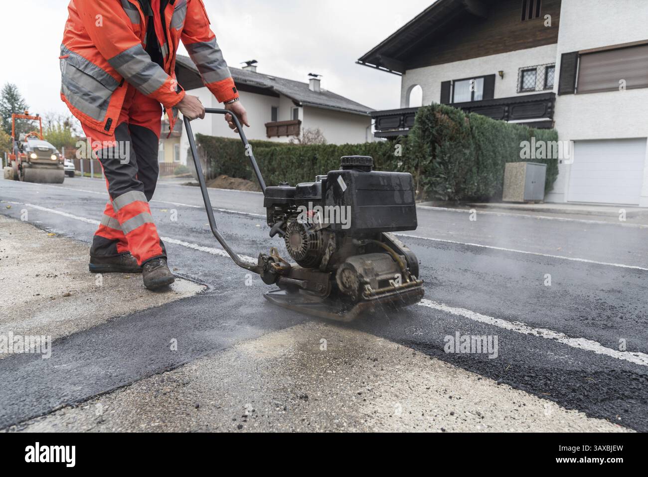 Lavoratore con piastra vibrante durante il lavoro di asfaltatura sulla pavimentazione Foto Stock