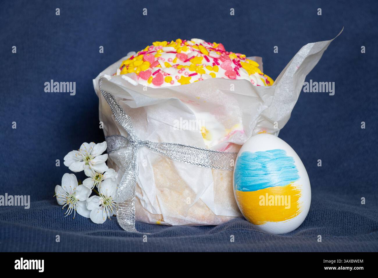 Uovo di Pasqua con bandiera Ucraina dipinta, kulich e ramoscello di ciliegio in fiore su sfondo blu, Pasqua in Ucraina Foto Stock