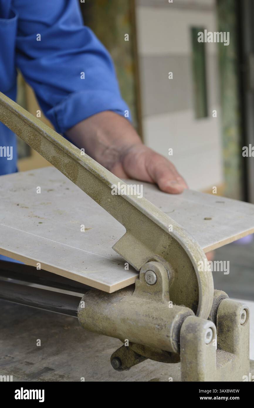 I lavoratori qualificati tagliano e spezzano le piastrelle alla giusta dimensione Foto Stock