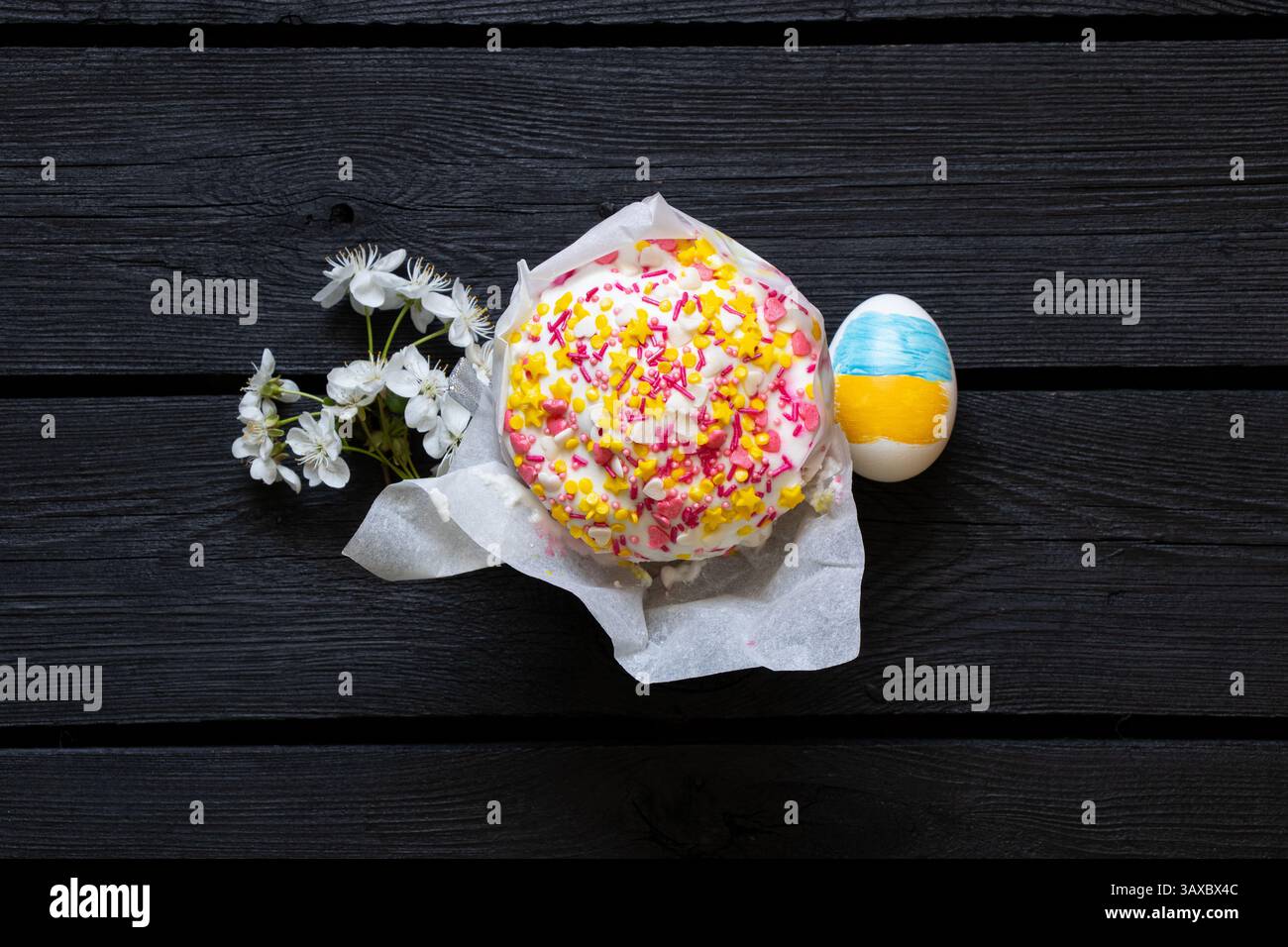 Uovo di Pasqua con bandiera Ucraina dipinta, kulich e ramoscello di ciliegio in fiore su un tavolo di legno nero, Pasqua in Ucraina Foto Stock