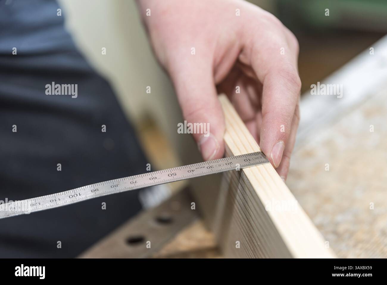 Il carpentiere misura lo spessore del pannello di legno con metro a nastro - primo piano della stazione di lavoro del carpentiere Foto Stock