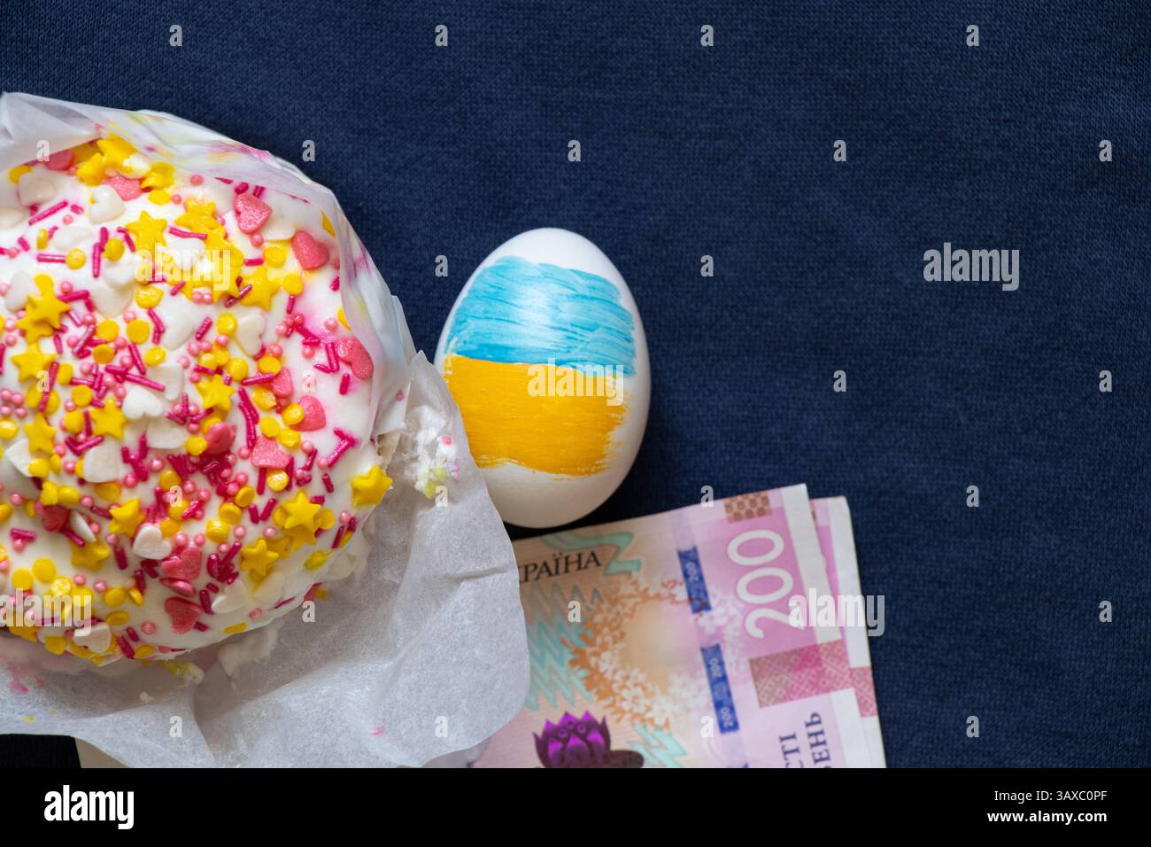Torta di Pasqua e duecento banconote di hrivnia e un uovo con la bandiera dell'Ucraina su sfondo blu, spese di Pasqua, spese e denaro Foto Stock