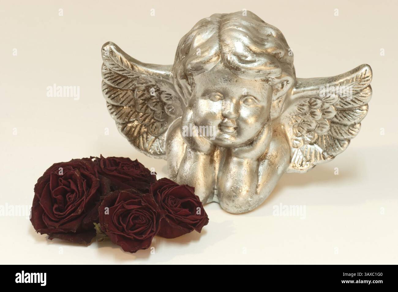 Angelo d'oro con rose rosse essiccate su sfondo di colore chiaro Foto Stock