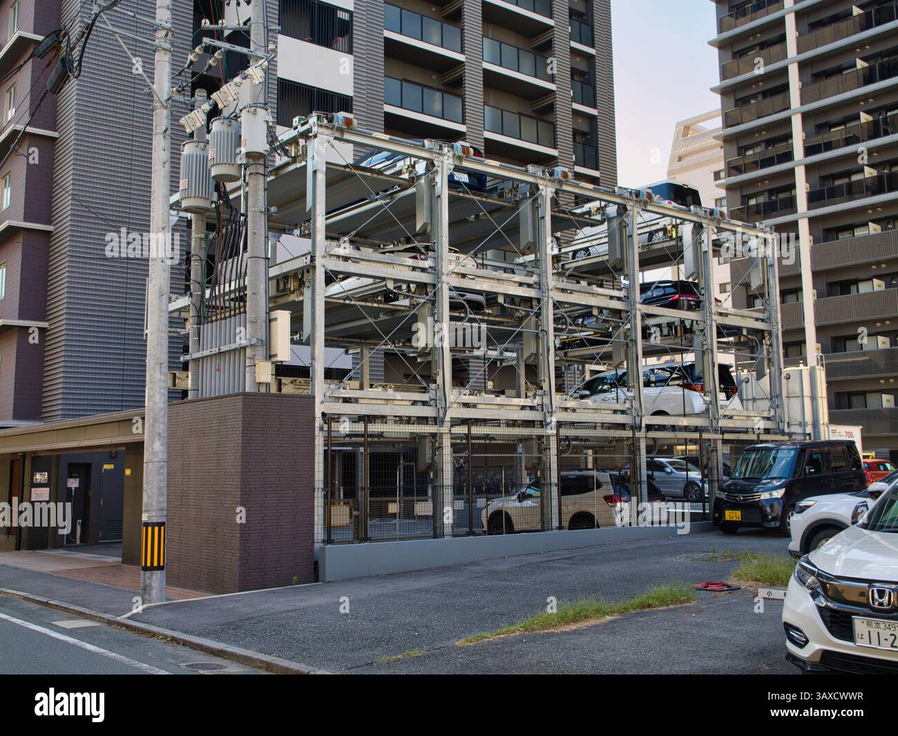 Sistema di parcheggio auto meccanizzato a Kyushu, Giappone, che consente di stoccare i veicoli in modo efficiente verticalmente per massimizzare lo spazio urbano limitato, circondato da un edificio moderno Foto Stock