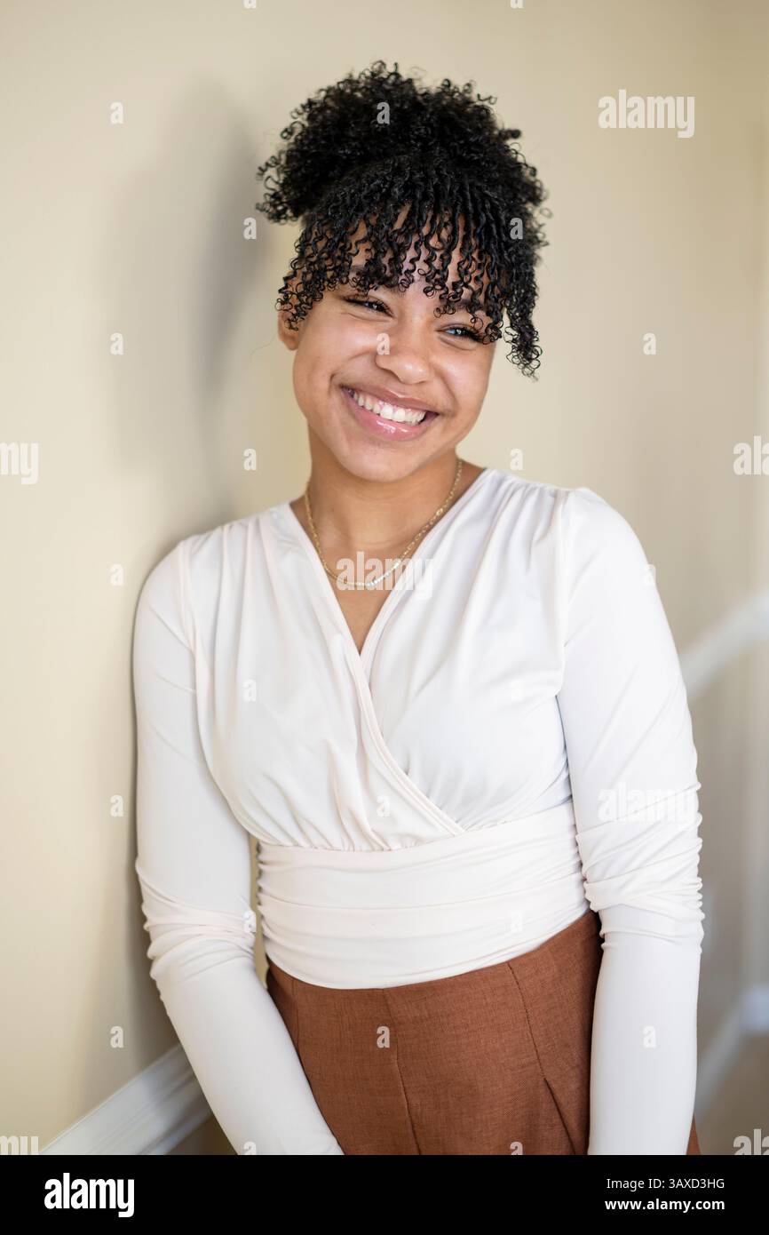 Donna sorridente in camicetta bianca si appoggia casualmente contro il muro Foto Stock