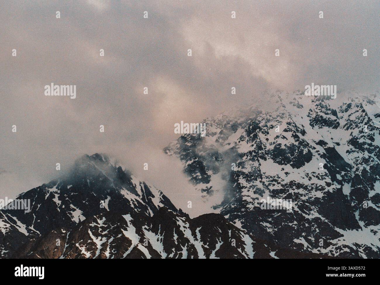 Le nuvole sospese attraversano le cime innevate di questa montagna Foto Stock