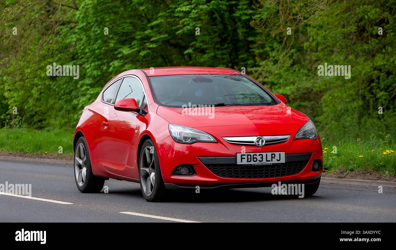 Milton Keynes, Regno Unito - 9 aprile 2025: 2014 auto Vauxhall Astra rossa che guida su una strada di campagna britannica Foto Stock Milton Keynes, Regno Unito - 9 aprile 2025: 2014 auto Vauxhall Astra rossa che guida su una strada di campagna britannica Foto Stock