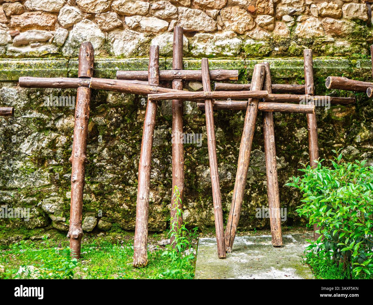 Rustiche croci in legno si aprono per la processione della via Crucis della settimana Santa, adagiata su un'antica parete in pietra con muschio e vegetazione. Foto Stock