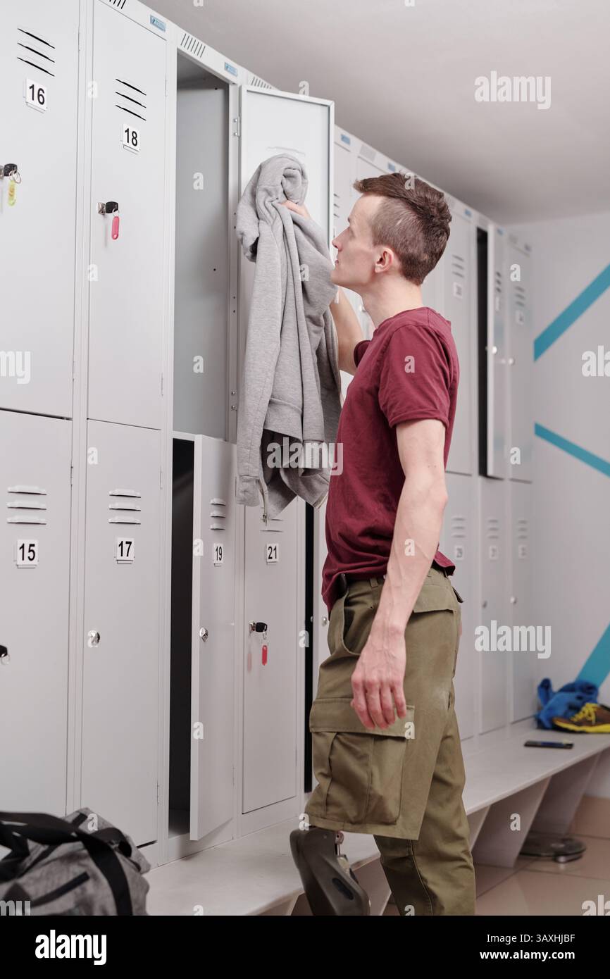 Giovane disabile in abbigliamento sportivo che guarda in un armadio aperto nello spogliatoio Foto Stock
