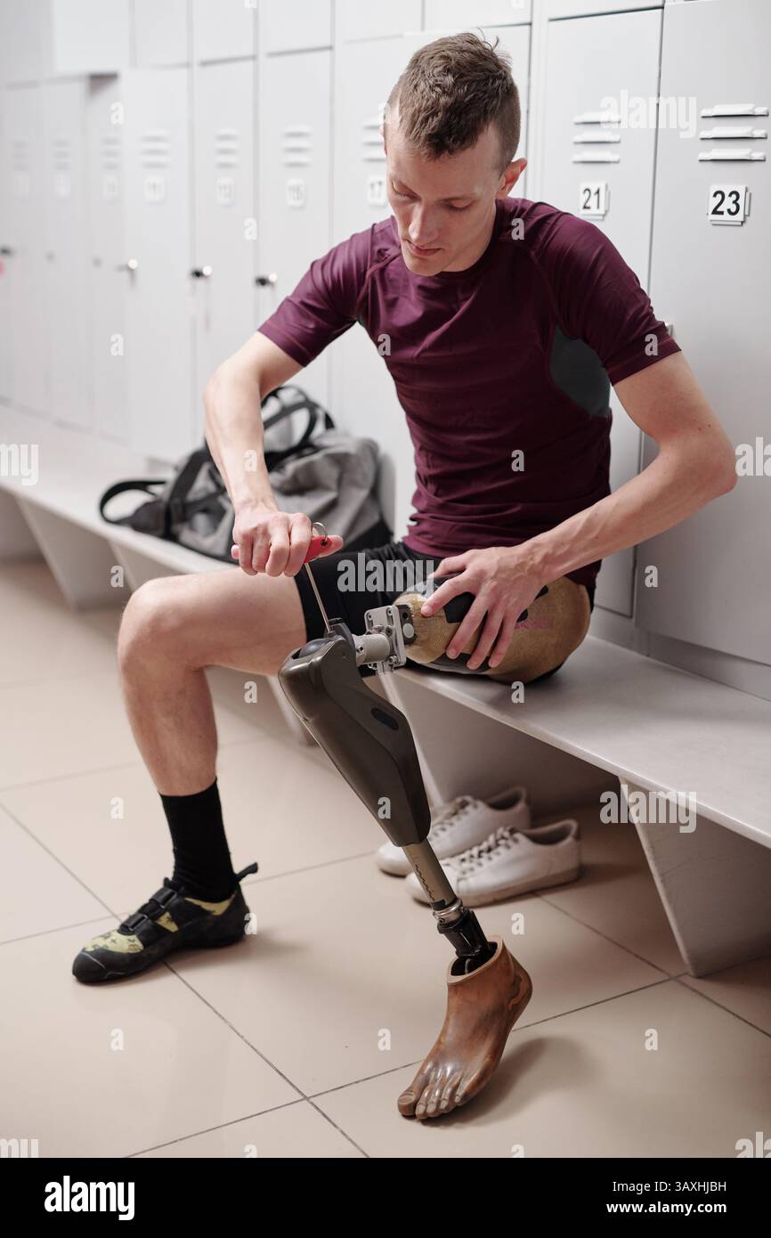 Giovane uomo disabile che fissa la protesi delle gambe seduto nello spogliatoio Foto Stock