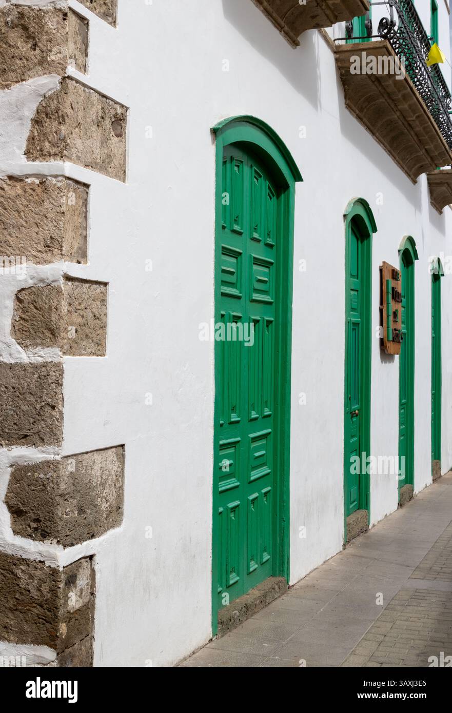 Facciata bianca di un vecchio edificio. Angolo in pietra decorativa. Quattro porte verdi brillanti. Aguimes, Las Palmas, Gran Canaria, Isole Canarie, Spagna. Foto Stock