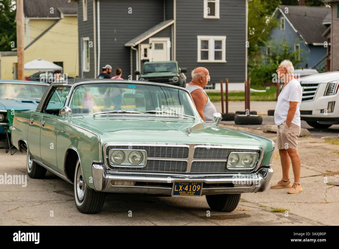 Un uomo si appoggia sul suo hardtop verde Chrysler Imperial a quattro porte del 1965 parcheggiato ad Auburn, Indiana, USA. Foto Stock