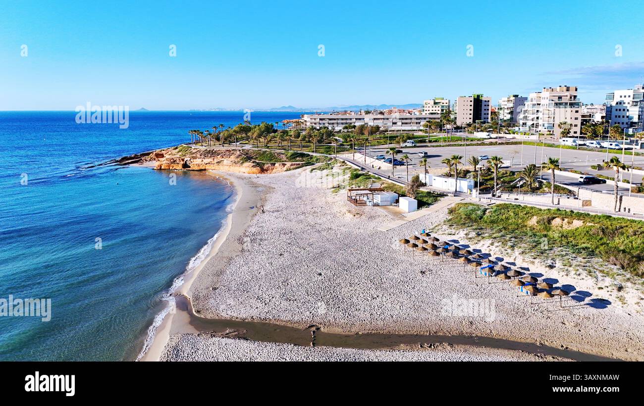 Vista aerea della costa di MIL Palmeras, che mostra le case sul lungomare, il lungomare, la spiaggia sabbiosa e il mare Mediterraneo turchese sotto il cielo azzurro Foto Stock