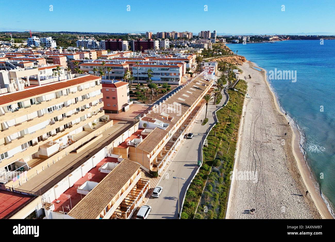 Vista aerea della costa di MIL Palmeras, che mostra le case sul lungomare, il lungomare, la spiaggia sabbiosa e il mare Mediterraneo turchese sotto il cielo azzurro Foto Stock