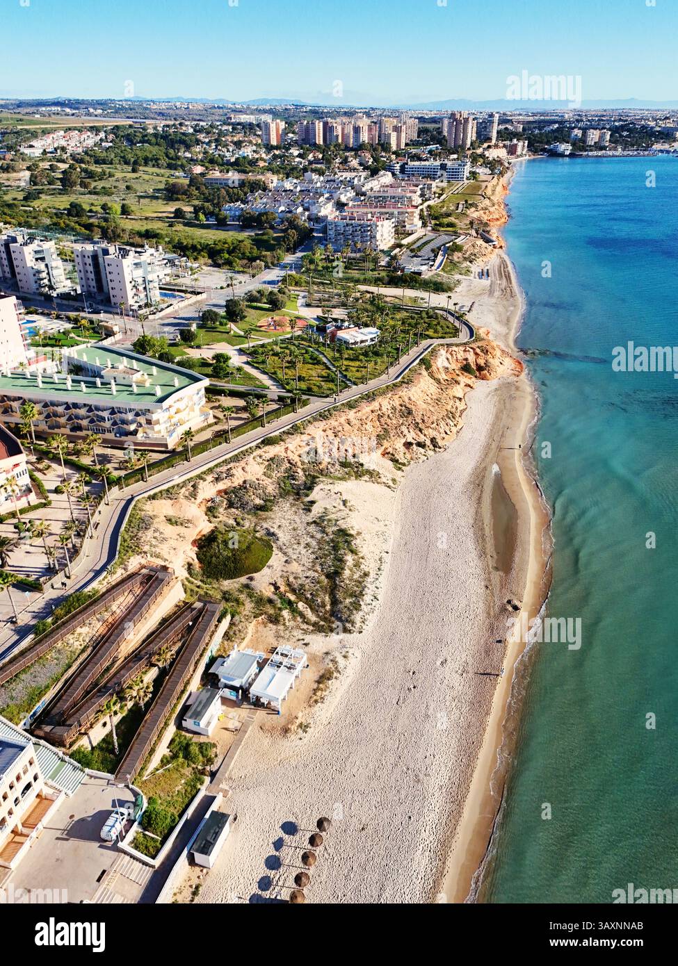 Vista aerea della costa di MIL Palmeras, che mostra le case sul lungomare, il lungomare, la spiaggia sabbiosa e il mare Mediterraneo turchese sotto il cielo azzurro Foto Stock