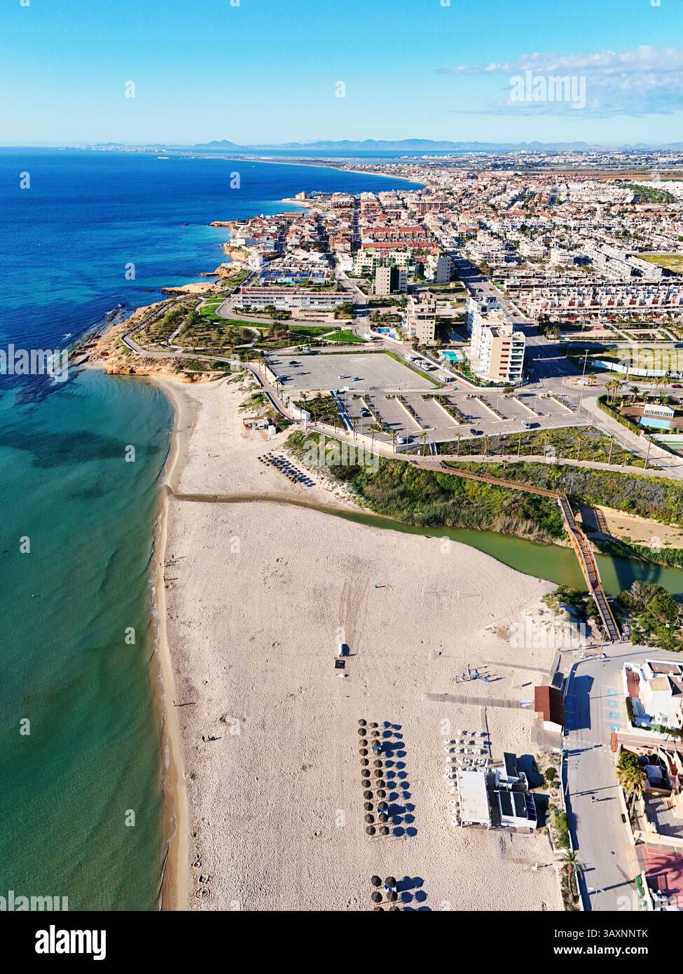 Vista aerea della costa di MIL Palmeras, che mostra le case sul lungomare, il lungomare, la spiaggia sabbiosa e il mare Mediterraneo turchese sotto il cielo azzurro Foto Stock