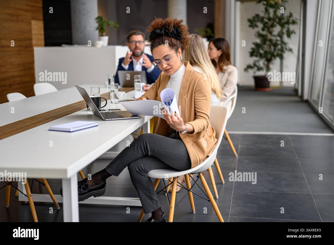 Donna d'affari che esamina i rapporti e lavora con i colleghi in background in un ufficio moderno Foto Stock
