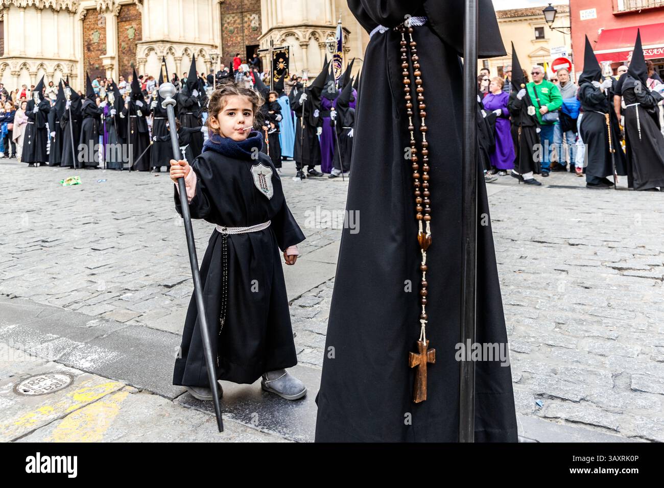 Anche i più piccoli partecipano alla processione del venerdì Santo EN el Calvario a Cuenca. Un bambino indossa abiti neri, tiene un bastone e succhia un lecca. Plaza Mayor, Cuenca, Castiglia-la Mancha, Spagna Foto Stock