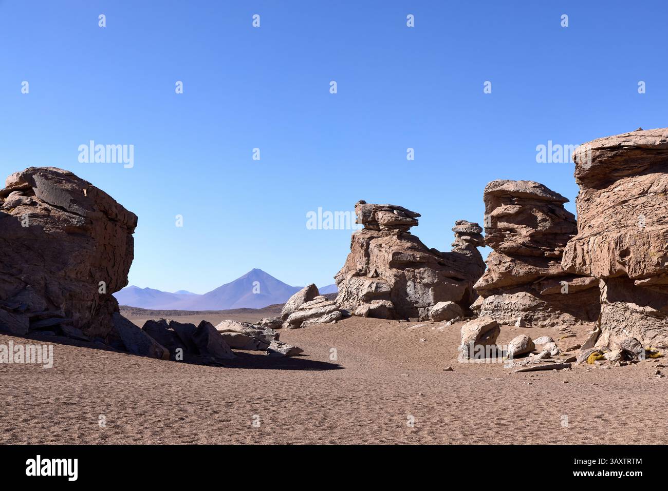 Formazioni rocciose intempestive e archi in pietra scolpiti dall'erosione del vento nel Parco Nazionale di Eduardo Avaroa, Bolivia. Cono vulcanico distante visibile attraverso il des Foto Stock