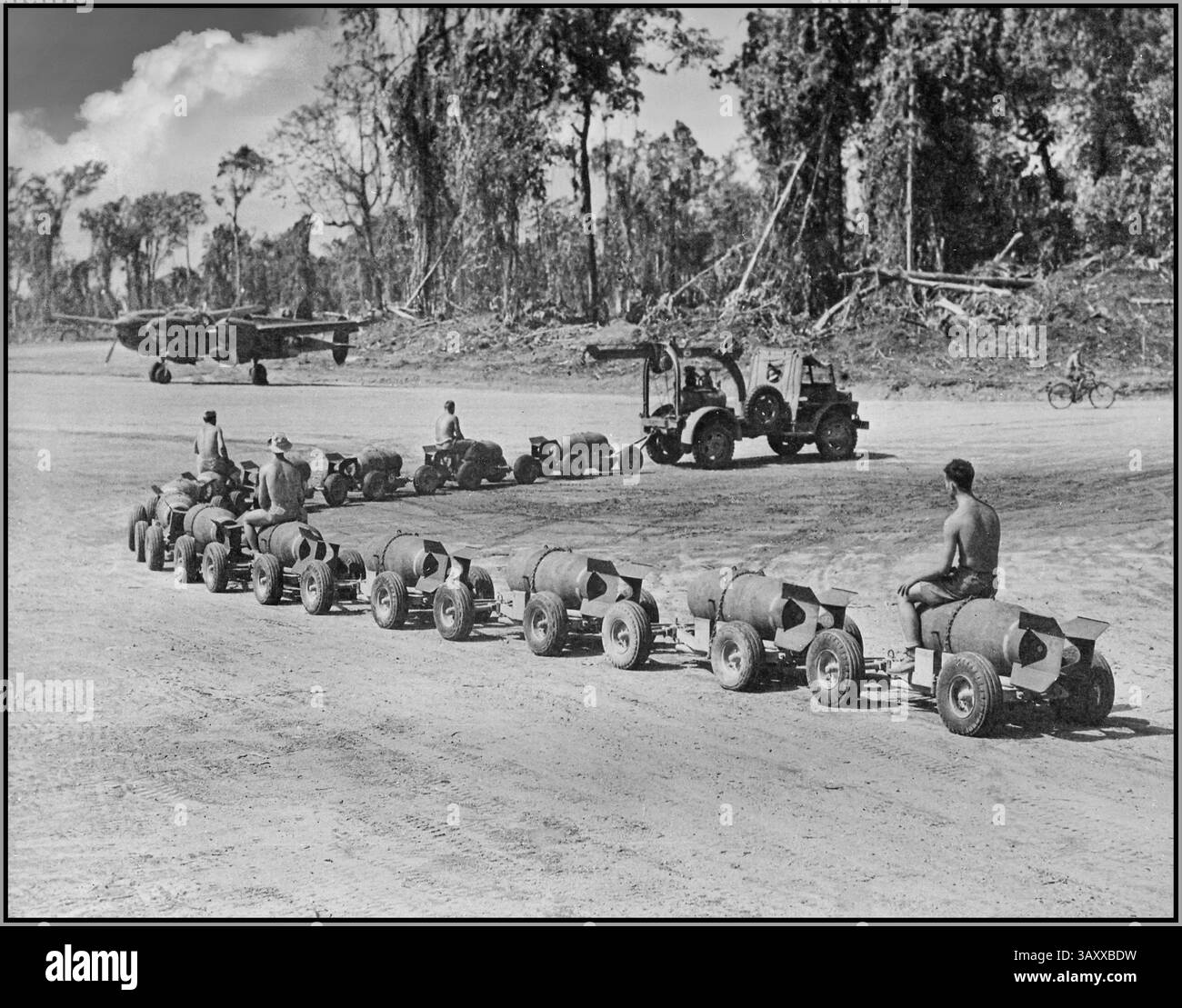 Manipolazione di bombe della seconda Guerra Mondiale nel Pacifico in una base avanzata del Pacifico. Bombe trainate ad un atteso B-25 Mitchell nordamericano , un bombardiere medio americano USAF utilizzato nella guerra del Pacifico contro il Giappone. Ford GTB "Burma Jeeps" che traina rimorchi di bombe in una base del Pacifico durante la seconda guerra mondiale veicolo: Ford GTB, un veicolo 4x4 da 1 1/2 tonnellate, noto anche come "Burma Jeep". Utilizzato per il traino e il riarmo di aeromobili nel Pacific Theater. Bombe: I rimorchi trasportano bombe da caricare sugli aeromobili. Aereo: Un bombardiere B-25 Mitchell è visibile sullo sfondo. Foto Stock