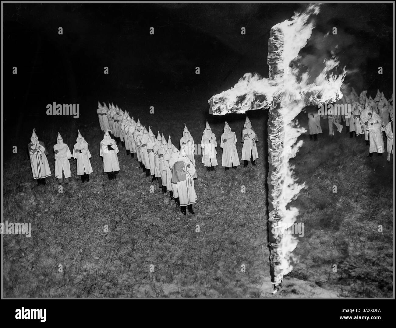 I membri del KKK del Ku Klux Klan, indossando tradizionali cappe bianche e abiti, stanno indietro a forma di Croce e guardano con le braccia incrociate dopo aver bruciato una croce di 15 piedi a Tampa, Flag., 30 gennaio 1939. Data 30 gennaio 1939 , i membri del Ku Klux Klan, indossando cappe e vesti bianche, guardano una croce in fiamme di notte a Tampa, Flag. STATI UNITI Foto Stock