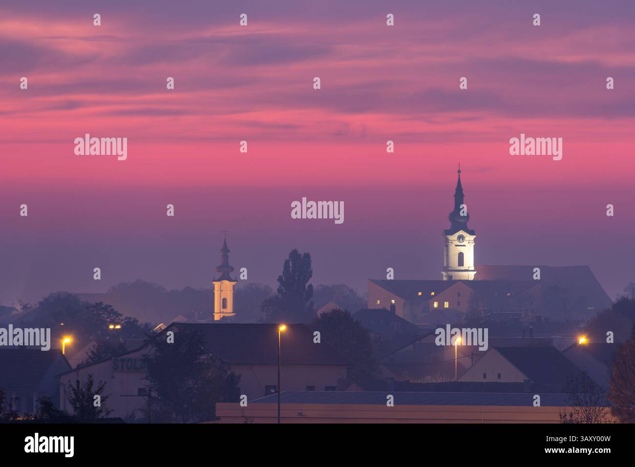 Tranquilla vista serale di un paesaggio urbano caratterizzato da torri e case della chiesa adagiate su un vibrante cielo al tramonto, evocando sentimenti di serenità e pace Foto Stock Tranquilla vista serale di un paesaggio urbano caratterizzato da torri e case della chiesa adagiate su un vibrante cielo al tramonto, evocando sentimenti di serenità e pace Foto Stock
