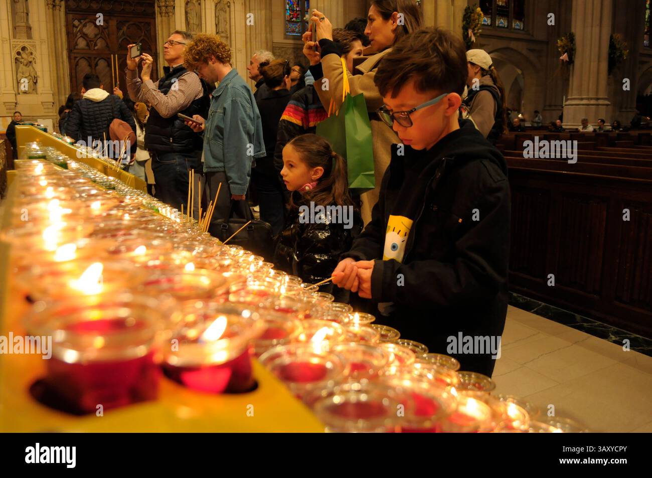 New York, Stati Uniti. 21 aprile 2025. I bambini accendono le candele nella cattedrale di San Patrizio. La cattedrale di San Patrizio ha tenuto una funzione commemorativa per Papa Francesco, morto lunedì 21 aprile all'età di 88 anni. I fedeli si riunirono nella cattedrale per rendere omaggio al defunto papa. La domenica di Pasqua, Papa Francesco ha salutato migliaia di fedeli in Piazza San Pietro. Il Vaticano ha detto che il papa è morto per un ictus che ha portato a coma e insufficienza cardiaca. (Foto di Jimin Kim/SOPA Images/Sipa USA) credito: SIPA USA/Alamy Live News Foto Stock