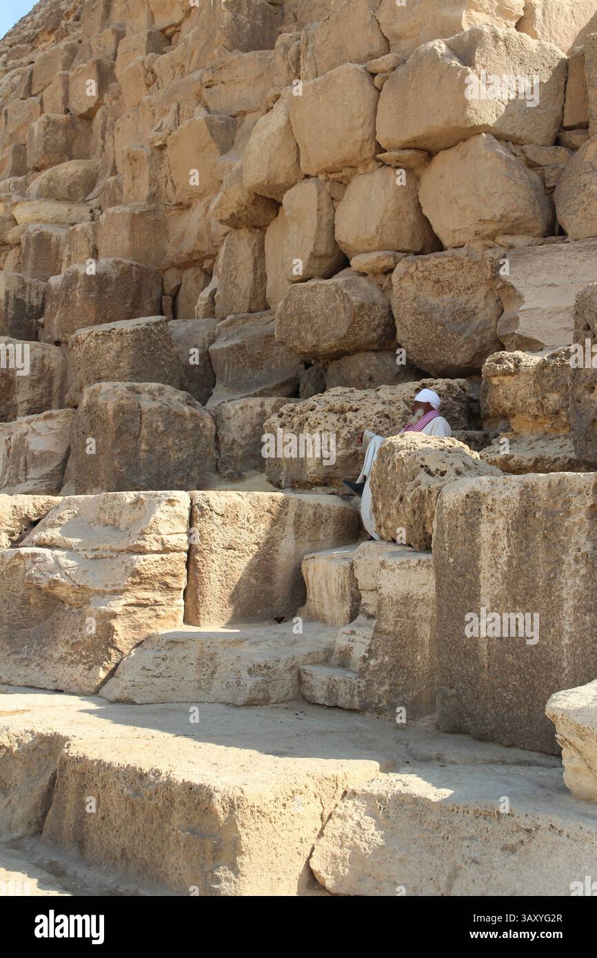 Giza, Egitto - 19 ottobre 2023: Un vecchio egiziano seduto su un blocco delle piramidi di Khufu Foto Stock