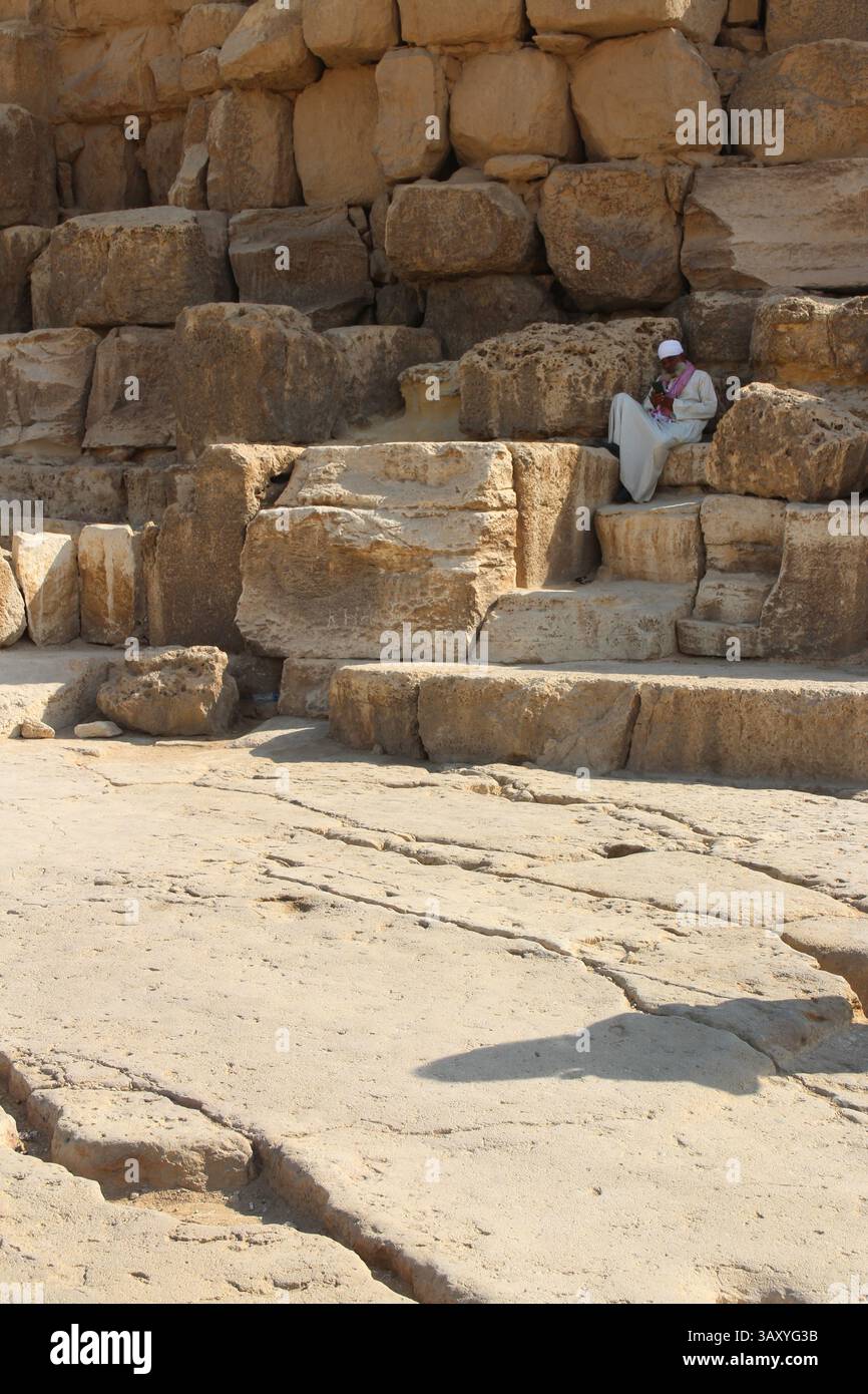 Giza, Egitto - 19 ottobre 2023: Un vecchio egiziano seduto su un blocco delle piramidi di Khufu Foto Stock