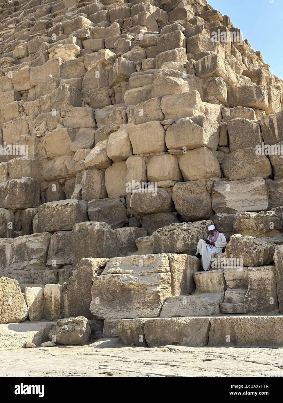 Giza, Egitto - 19 ottobre 2023: Un vecchio egiziano seduto su un blocco delle piramidi di Khufu Foto Stock