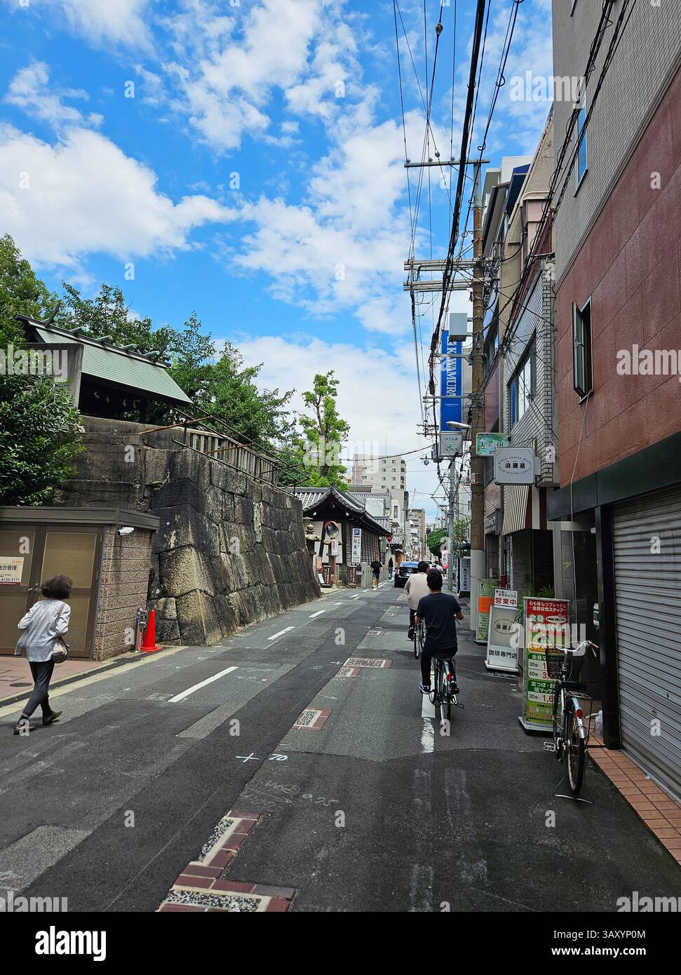 I ciclisti passano davanti al muro di pietra fuori dal Santuario Tenmangu di Osaka, Urban Street Scene, Osaka, Giappone Foto Stock