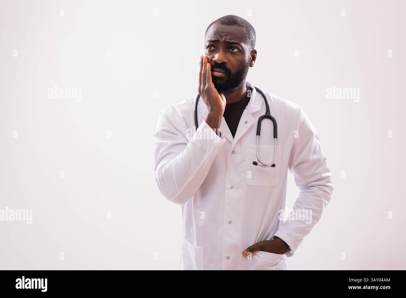 Ritratto di un paramedico maschile nero preoccupato che si sente preoccupato, che pensa e guarda lontano. Studio girato su sfondo grigio. Foto Stock