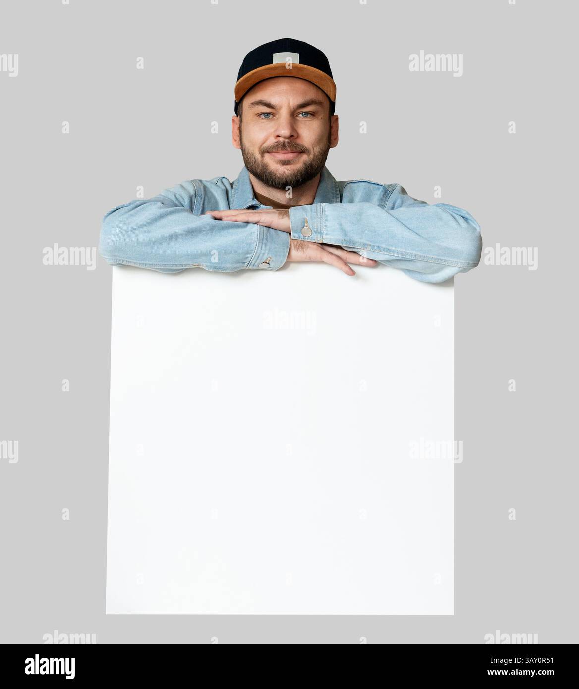 Un uomo sorridente isolato con lo schienale si appoggia su un poster bianco vuoto. Foto Stock