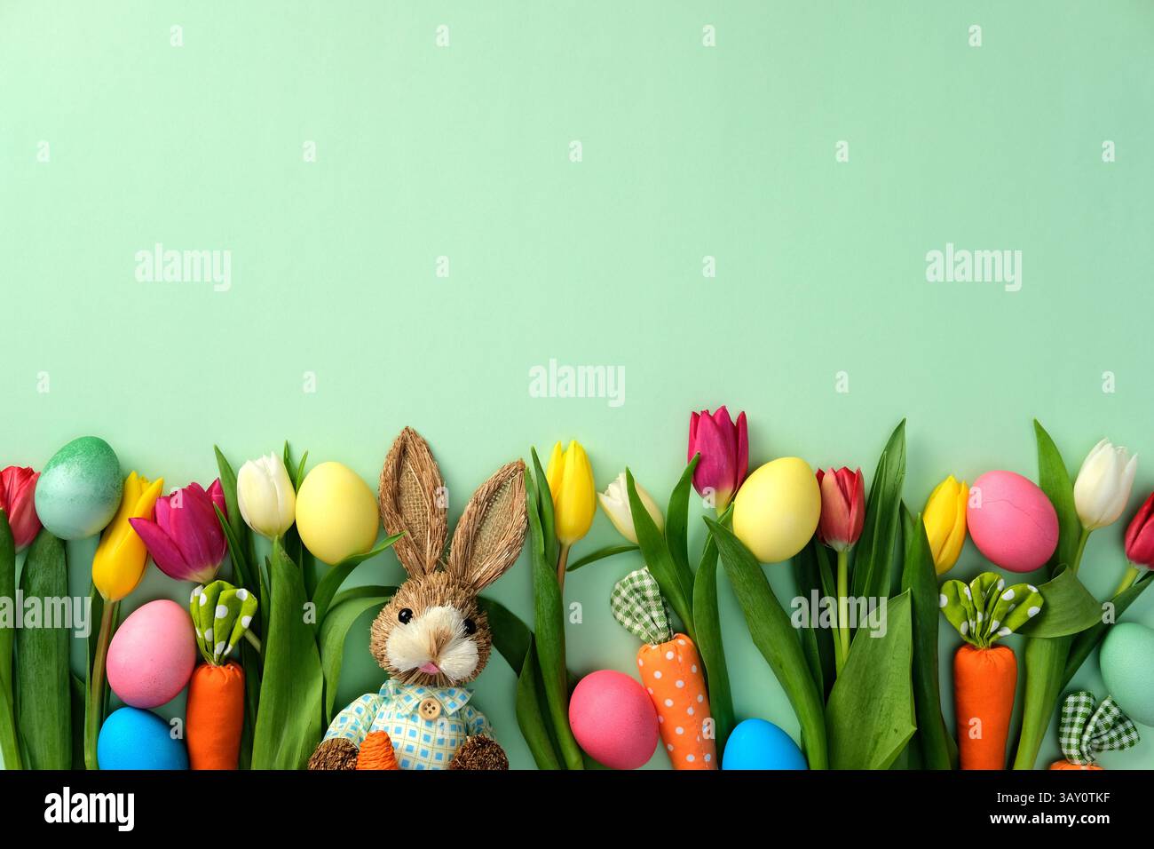 Design del biglietto di auguri di buona Pasqua. Deporre in piano uova di Pasqua colorate, carote decorative, tulipani e coniglietto su sfondo verde Foto Stock