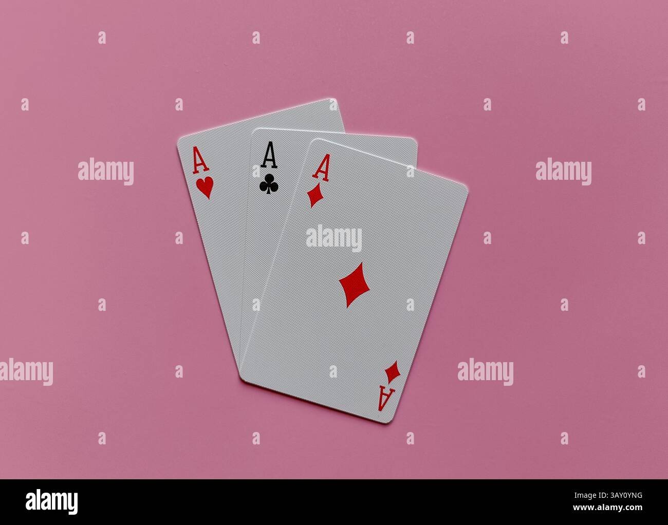 Tre carte da gioco, tutti gli assi, disposte su un morbido sfondo rosa. Ogni carta mostra un abito diverso: Cuori, mazze e diamanti. Foto Stock