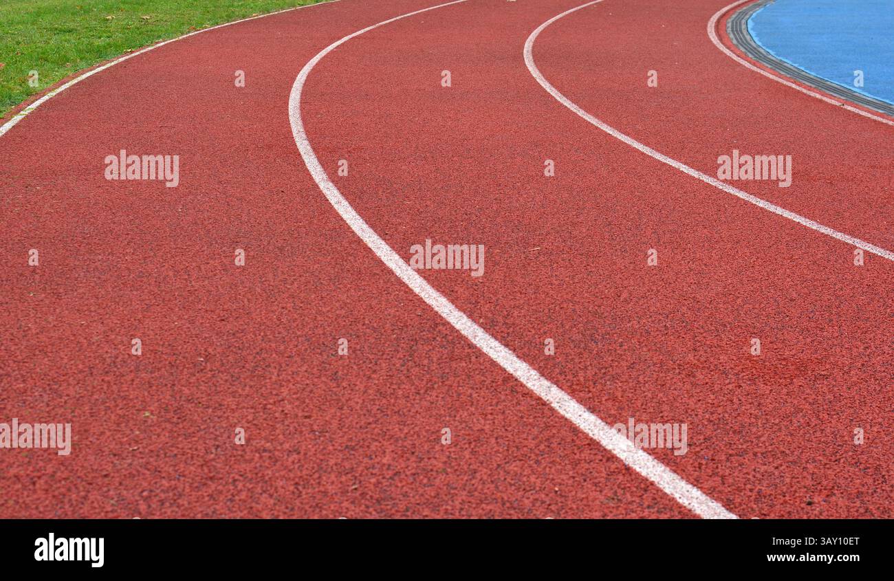 curva rossa della pista da corsa con linee bianche e erba verde sul lato destro Foto Stock