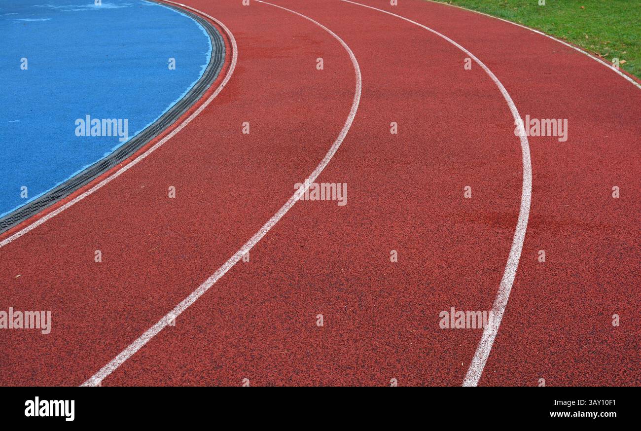 curva rossa della pista da corsa con linee bianche, campo sportivo blu sul lato sinistro e erba verde sul lato destro Foto Stock