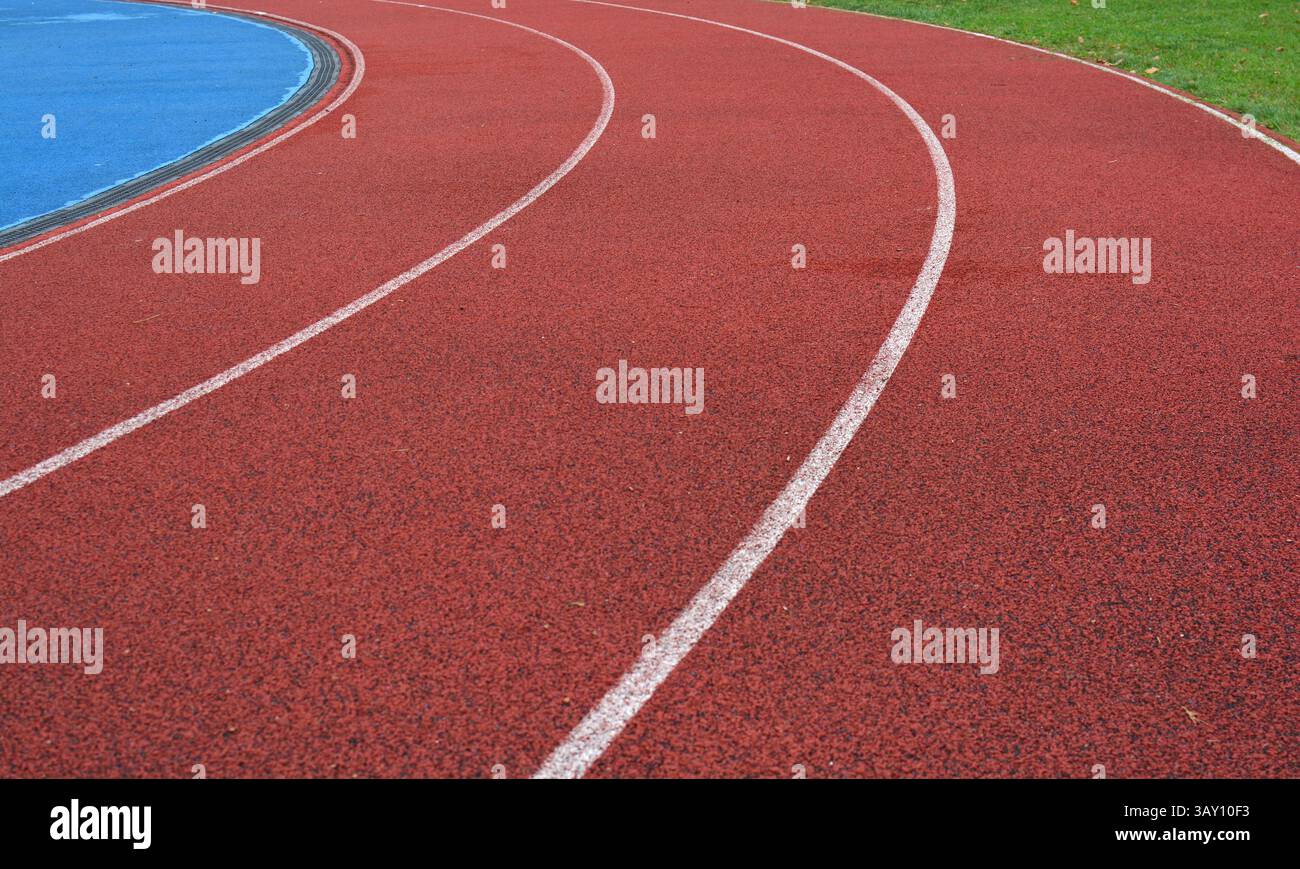 curva rossa della pista da corsa con linee bianche, campo sportivo blu sul lato sinistro e erba verde sul lato destro Foto Stock