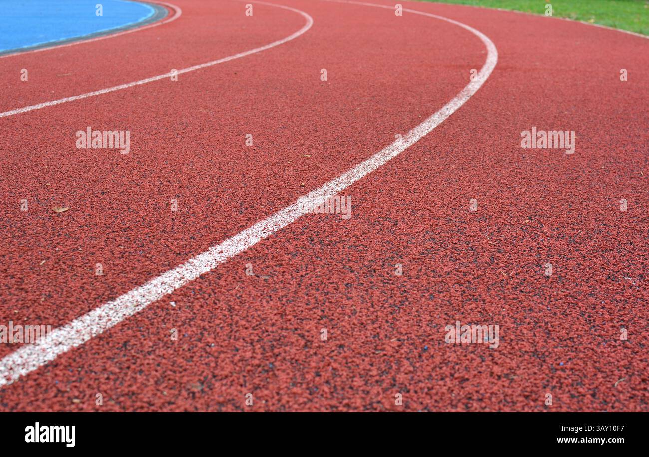 curva rossa della pista da corsa con linee bianche, campo sportivo blu sul lato sinistro e erba verde sul lato destro Foto Stock