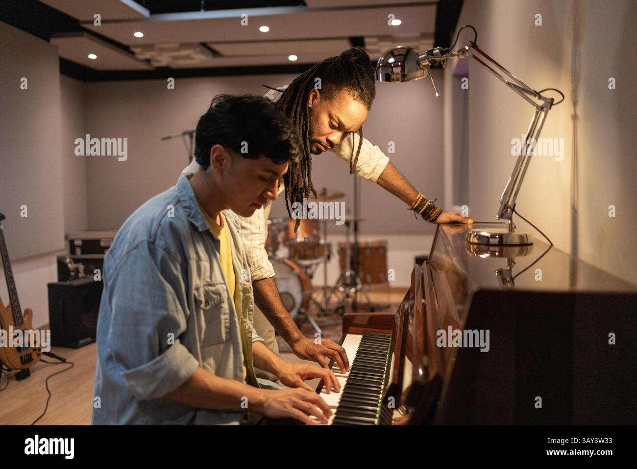 Due musicisti lavorano insieme al pianoforte, collaborando in modo creativo in un moderno studio di registrazione. Strumenti e attrezzature sono in background, Highli Foto Stock