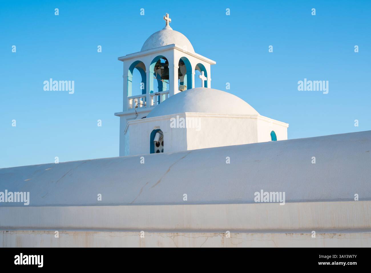 Vista accattivante di una tradizionale cupola della chiesa imbiancata di bianco con un campanile, adagiata su un cielo azzurro limpido a Triovasalos, Isola di Milos, Grecia. Una sere Foto Stock