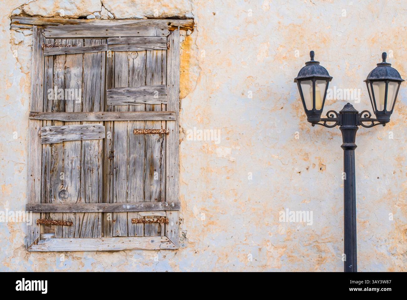 Un'antica finestra in legno e un lampione stradale vintage su una parete rustica e intemprata a Triovasalos, l'isola di Milos, in Grecia, mostrano l'intramontabile ch della zona Foto Stock