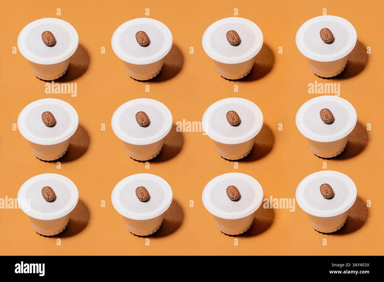 Una griglia di cialde biodegradabili disposte in modo ordinato, ciascuna con un chicco di caffè, su un vivace sfondo arancione. L'immagine evidenzia Foto Stock
