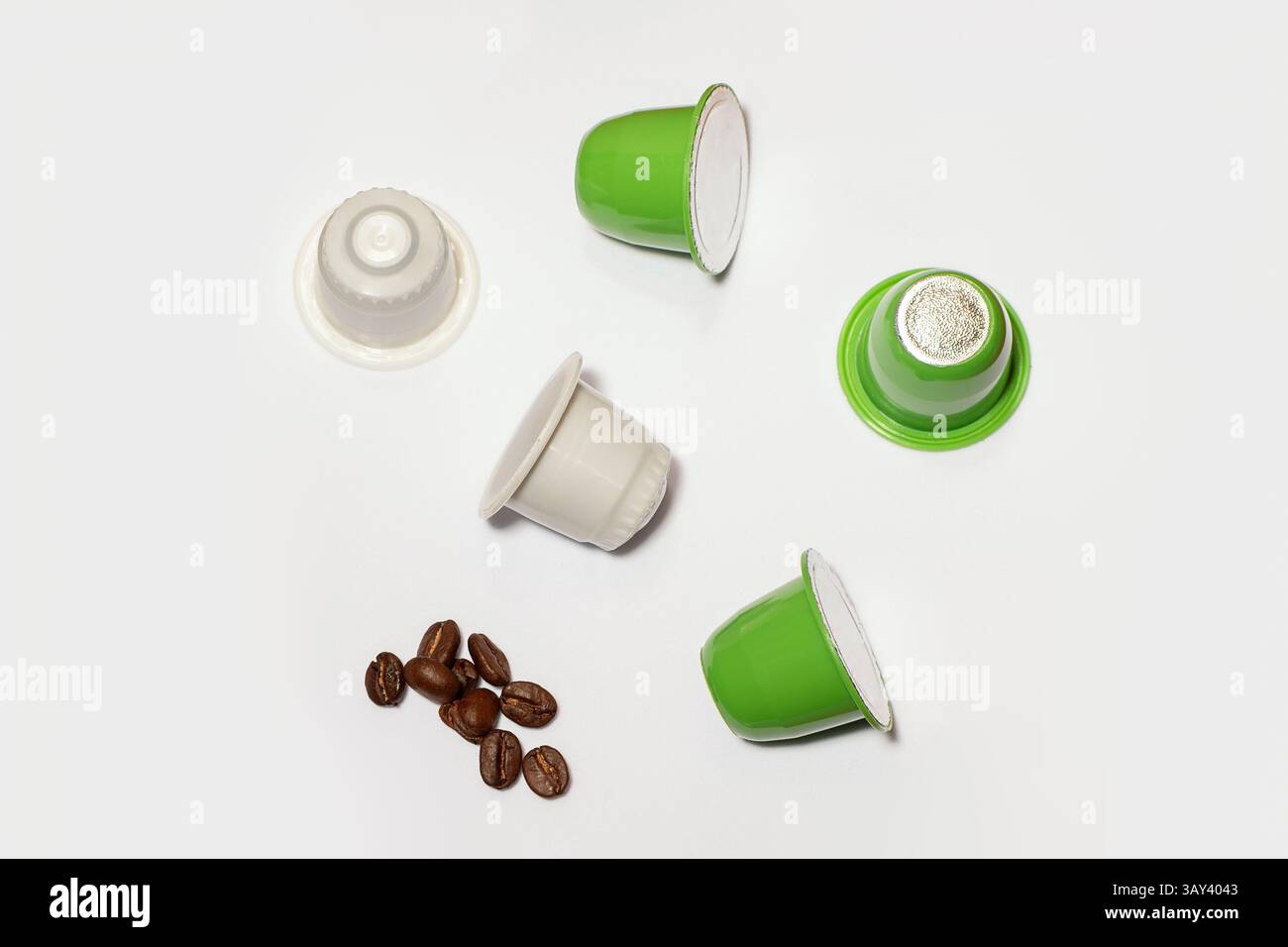 Una collezione di capsule di caffè biodegradabili verdi e bianche con chicchi di caffè sparsi su sfondo bianco. Questa immagine illustra la semplicità e la modernità Foto Stock