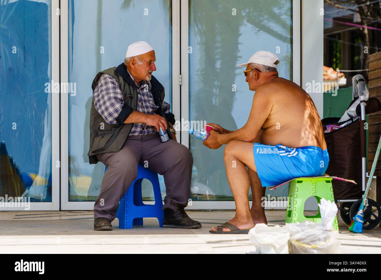 Maggio 2024. Durazzo, Albania. Due anziani che parlano all'ombra. Uno ha una lattina di birra, l'altro una bottiglia d'acqua. Foto: © Simon Grosset Foto Stock