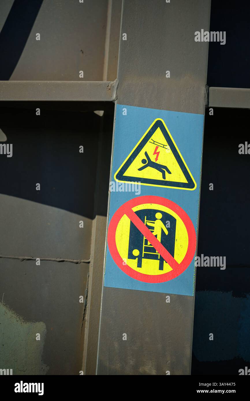 Due segnali sono visualizzati su un palo metallico in una zona di costruzione. Uno avverte dei pericoli elettrici con un simbolo di pericolo, mentre l'altro proibisce le salite Foto Stock