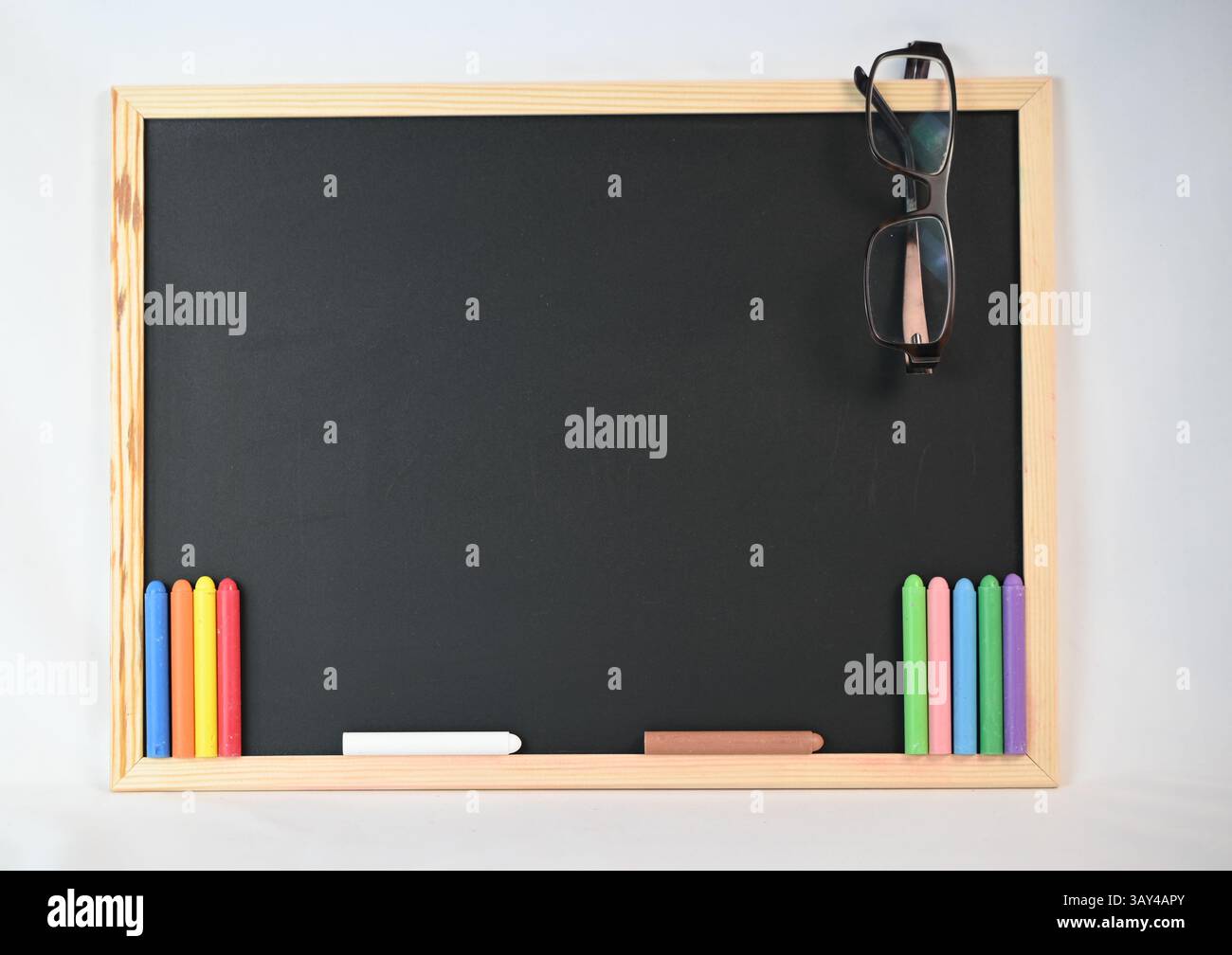Una lavagna tradizionale con pastelli colorati e occhiali appoggiati sulla superficie, pronta per l'uso in attività creative o per l'apprendimento Foto Stock